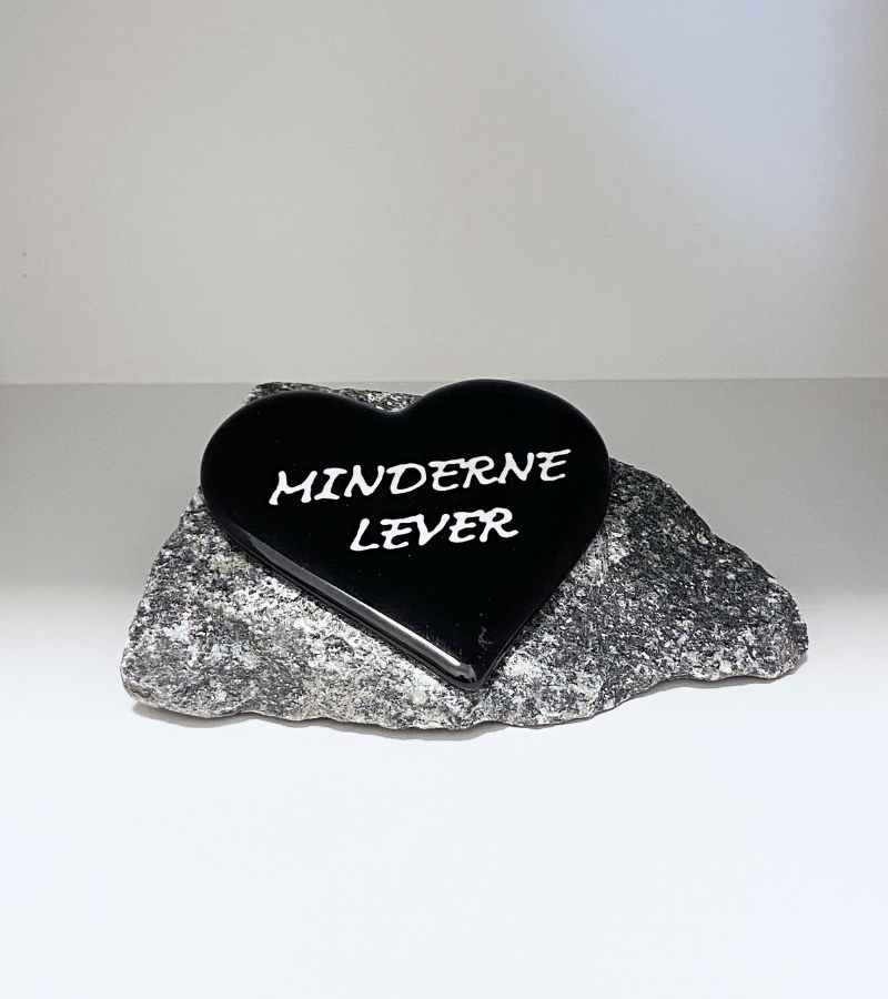 Minner lever, svart glasshjerte på granittstein